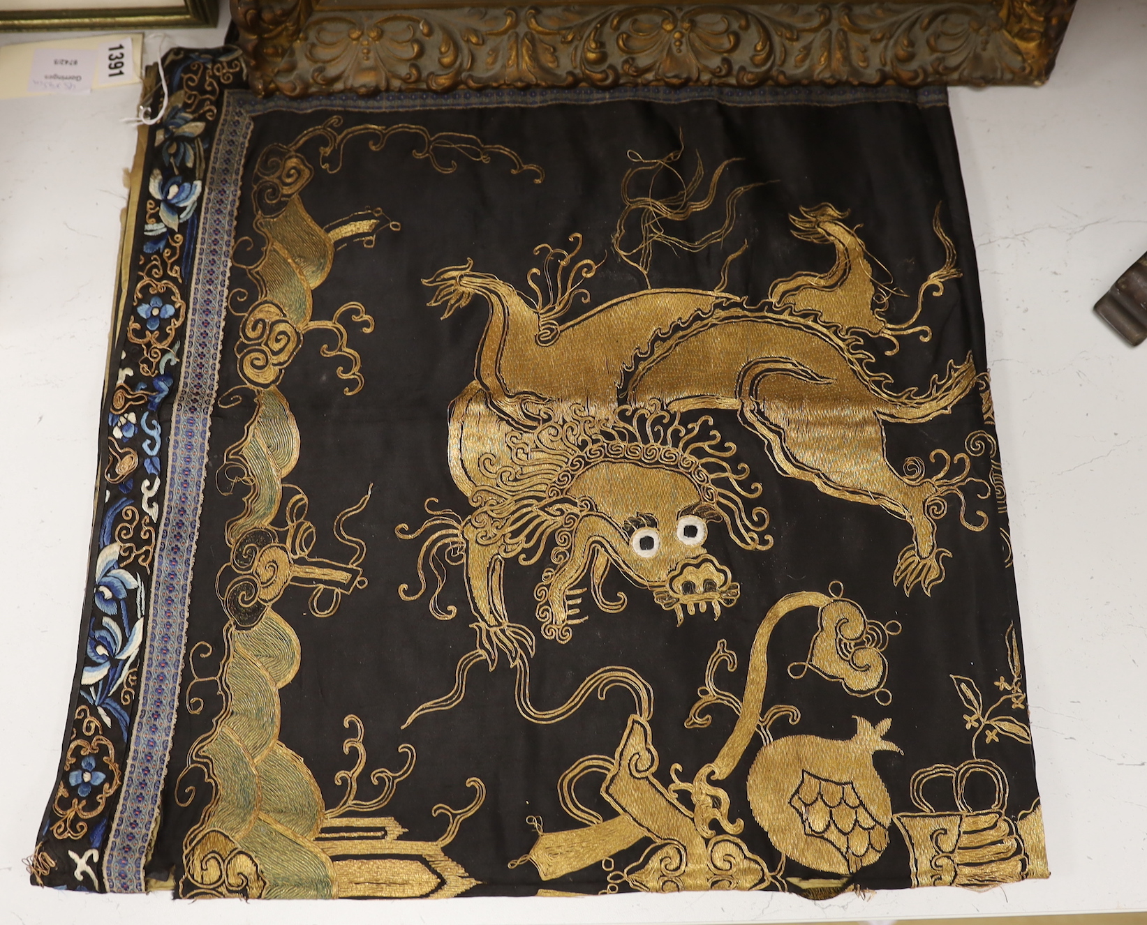 A 19th century Chinese dark blue ground panel, gilt thread embroidered with a pair of celestial dragons flying amongst precious objects, beneath a frieze, 95 x 95cm